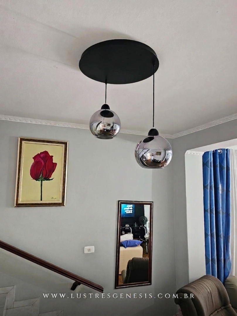 Lustre pendente Sarvah com 3 globos de vidro, instalado em sala de estar pr&oacute;xima &agrave; escada, destacando design moderno e sofisticado.
